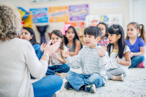 Young children sitting on floor in classroom listening to teacher.